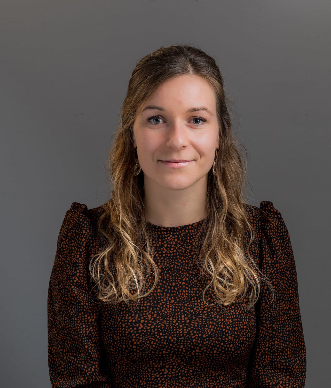 Lächelnde junge Frau in gepunktetem Kleid mit langen welligen Haaren, Studio-Porträt