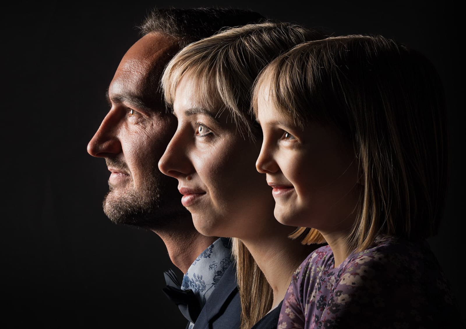 Profil-Porträt einer dreiköpfigen Familie nebeneinander in warmem Seitenlicht