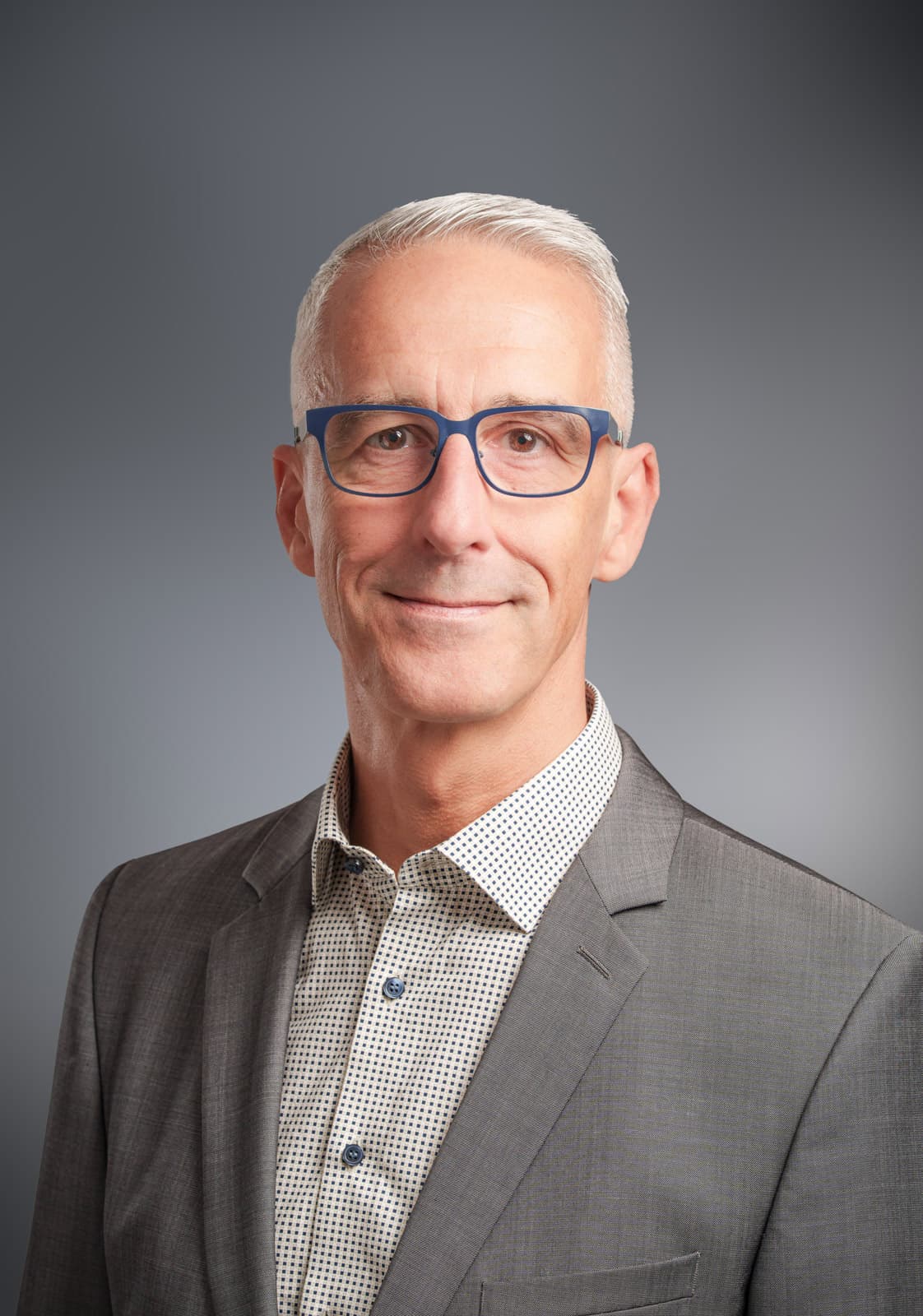 Älterer Geschäftsmann mit blauer Brille, grauem Sakko und kariertem Hemd