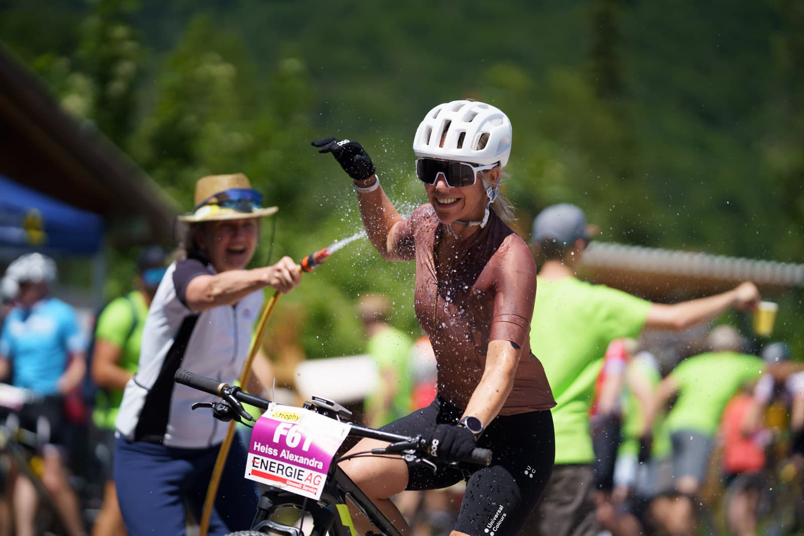 Lachende Mountainbikerin wird im Rennen mit einem Wasserschlauch abgekühlt