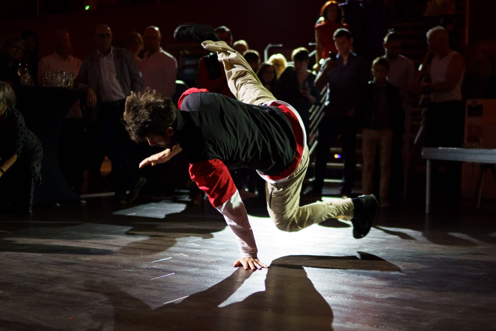 Breakdancer in akrobatischer Bodenpose vor schummrig beleuchtetem Galapublikum