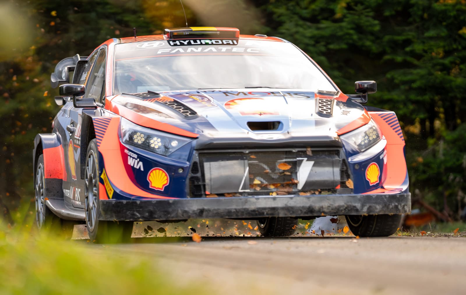 Frontansicht eines WRC-Hyundai-Rallyeautos beim Anbremsen, Laub wirbelt unter dem Wagen