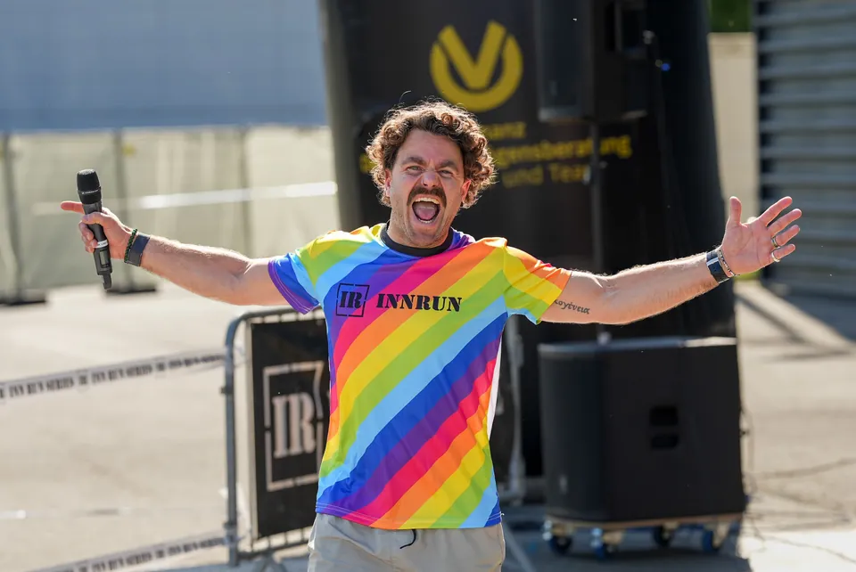 Teilnehmer im regenbogenfarbenen Shirt jubelt mit ausgebreiteten Armen.