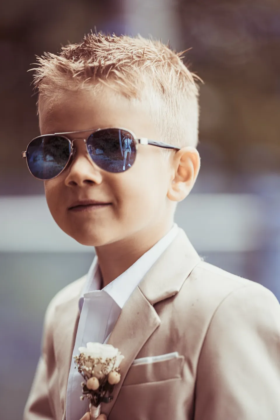 Junge im hellen Anzug mit Sonnenbrille und Blumenanstecker.