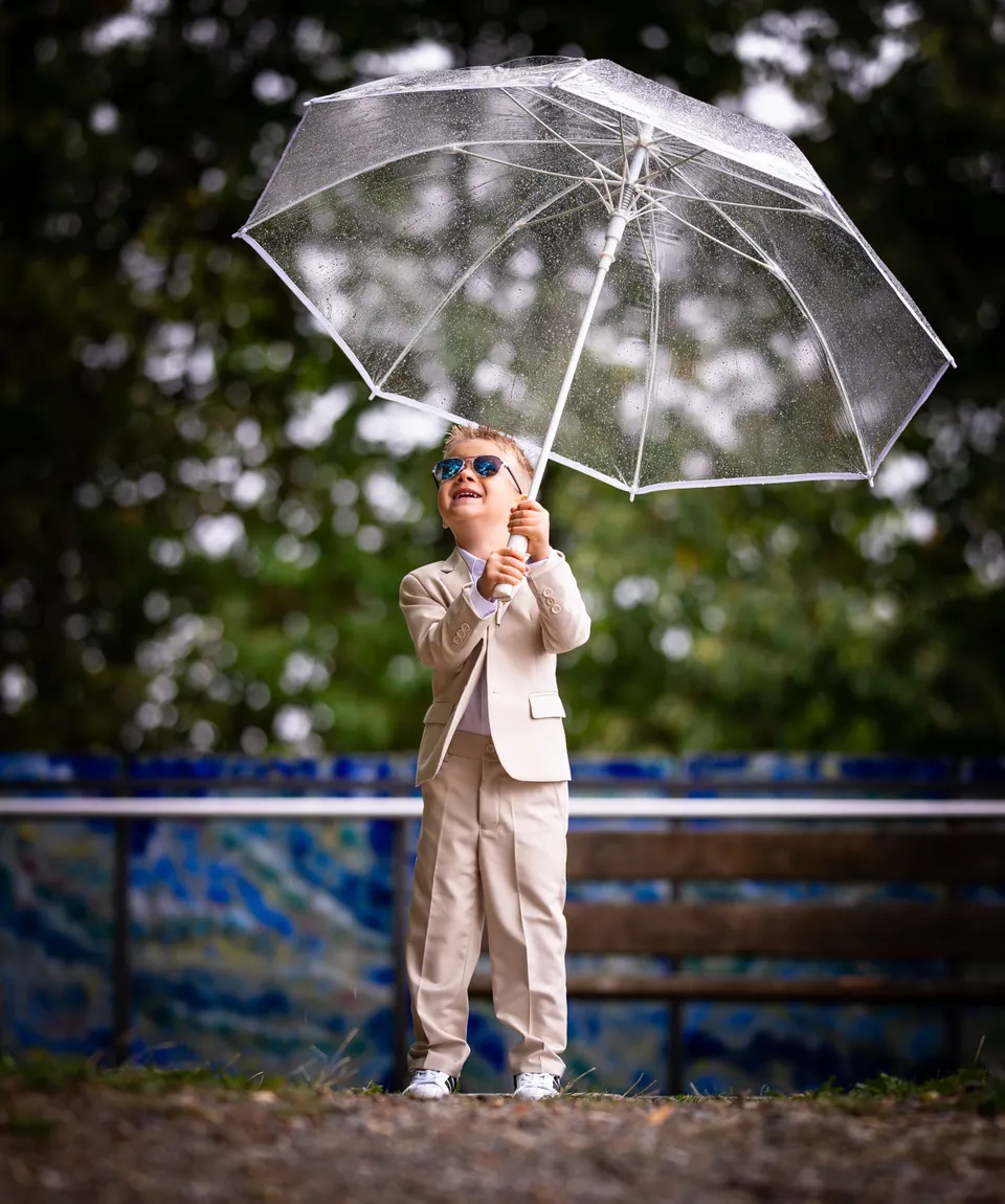 Junge im hellen Anzug hält einen durchsichtigen Regenschirm.
