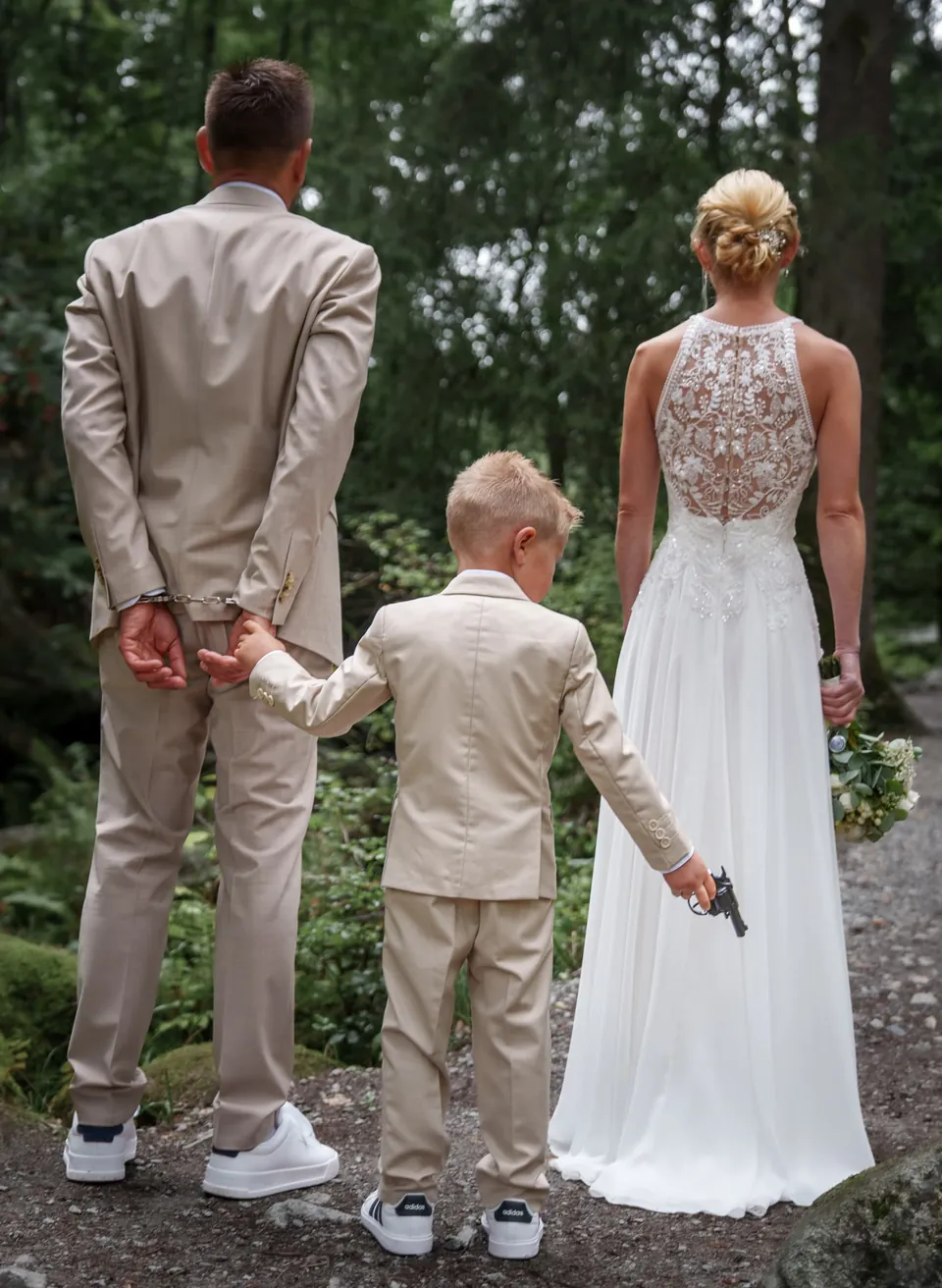 Brautpaar und Kind im hellen Anzug von hinten, Hand in Hand.