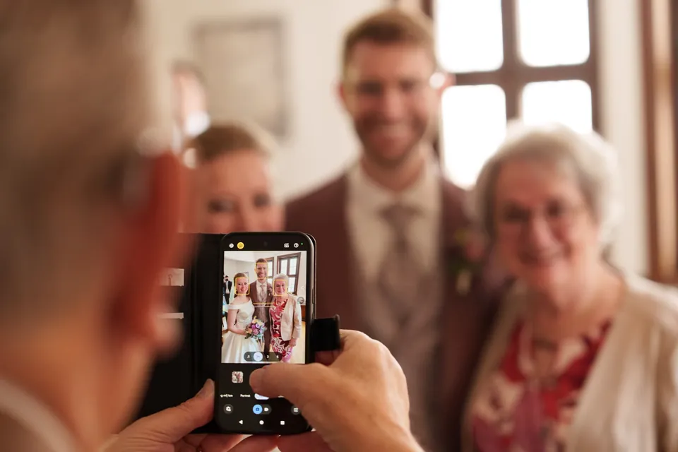 Ein Gast fotografiert eine Hochzeitsgruppe mit dem Smartphone.