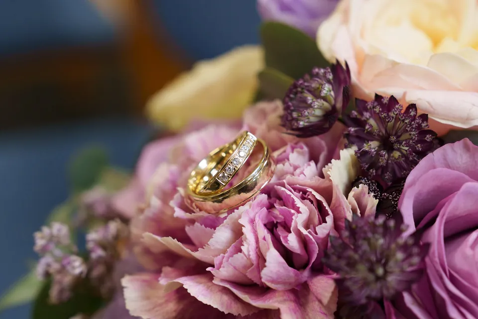 Zwei goldene Eheringe auf violetten Blüten des Brautstraußes.