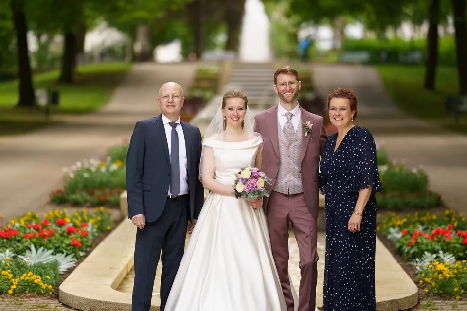 Vier Personen einer Hochzeitsgruppe stehen vor einem Blumenbeet im Park.